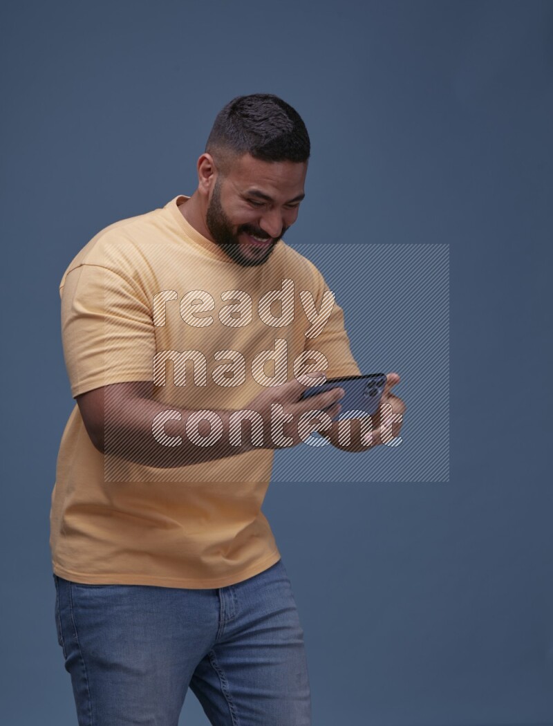 A man Playing Games on Smartphone on Blue Background wearing Orange T-shirt