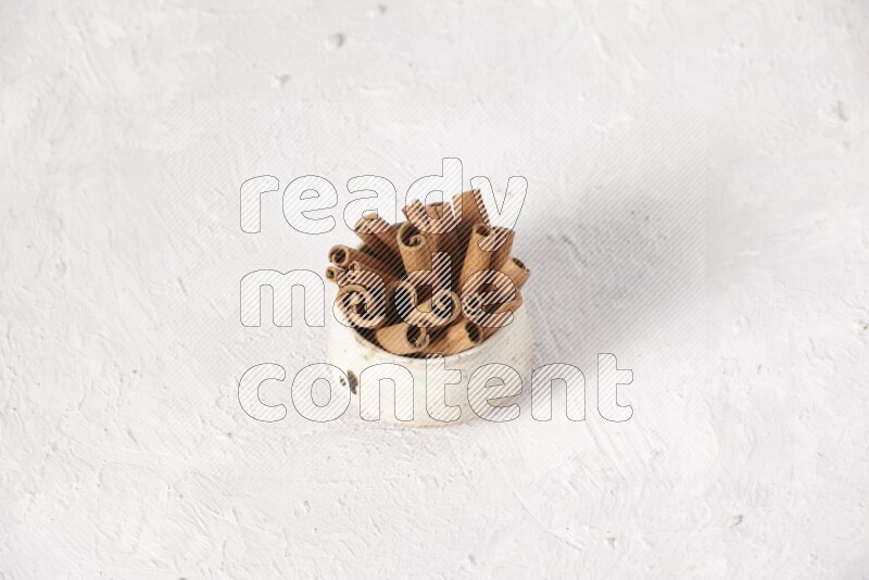Cinnamon sticks in a beige bowl on a white background