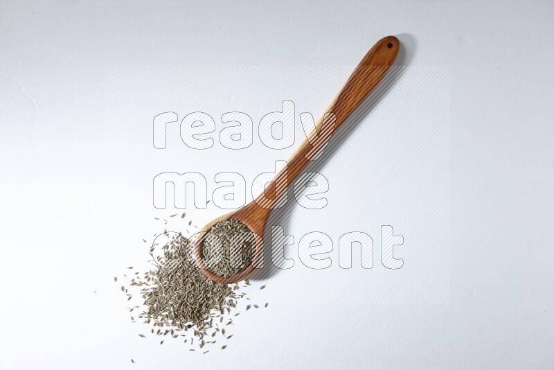 A wooden ladle full of cumin seeds on a white flooring