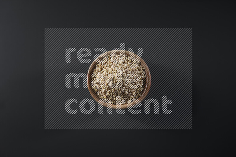 Hulled wheat in a wooden bowl on grey background