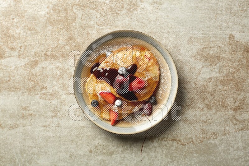 Three stacked mixed berries pancakes in a bicolor plate on beige background