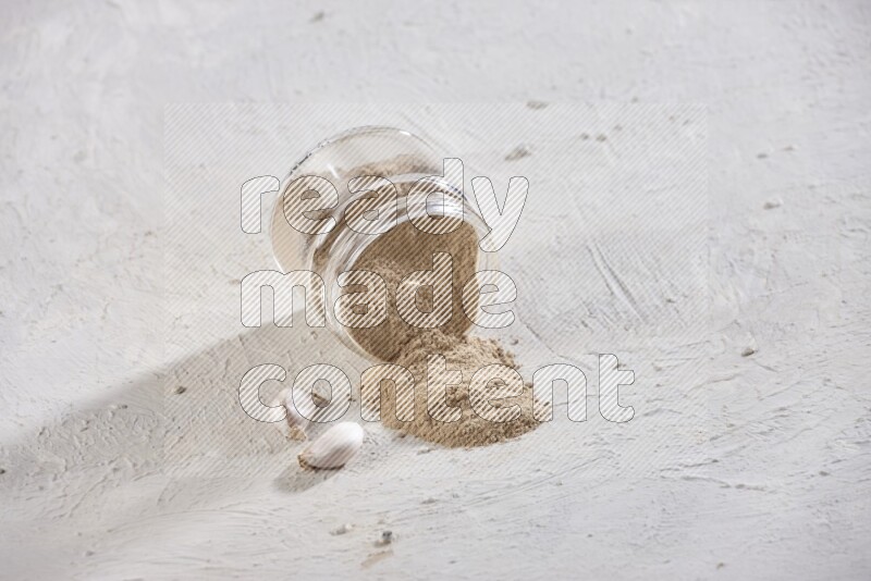 A glass jar full of garlic powder flipped over with the powder came out on a textured white flooring
