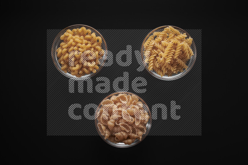 Different pasta types in glass bowls on black background