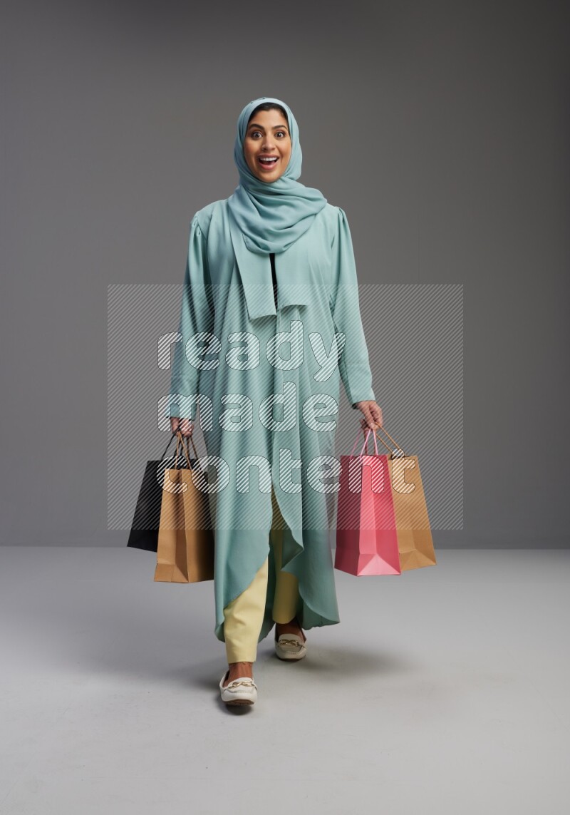 Saudi Woman wearing Abaya standing holding shopping bag on Gray background