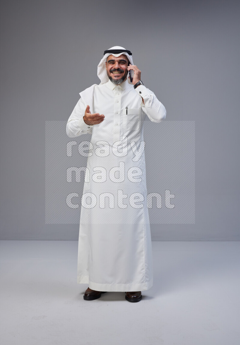 Saudi man Wearing Thob and white Shomag standing talking on phone on Gray background