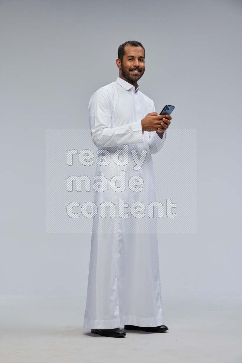 Saudi man wearing Thob standing texting on phone on Gray background