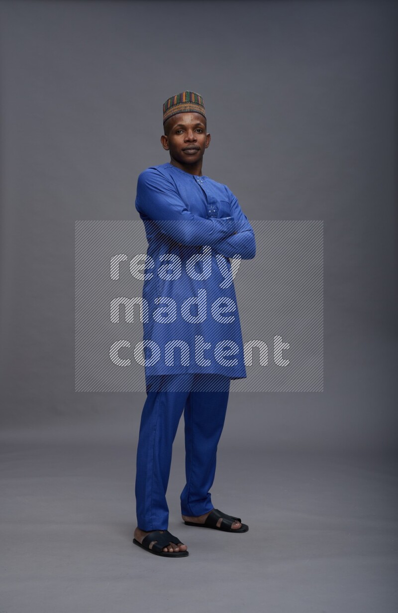 Man wearing Nigerian outfit standing with crossed arms on gray background