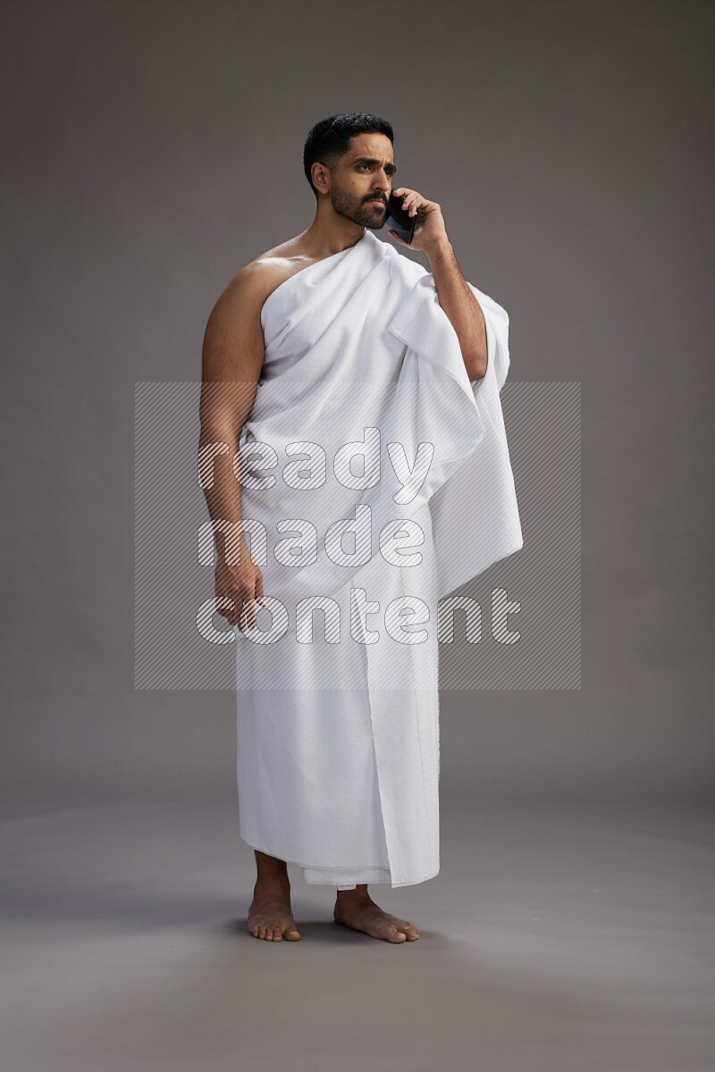 A man wearing Ehram Standing talking on phone on gray background