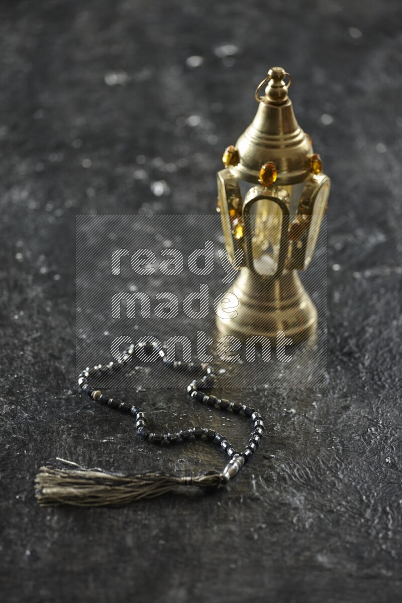 A golden lantern with different drinks, dates, nuts, prayer beads and quran on textured black background