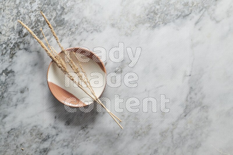 Wheat stalks on multicolored pottery plate on grey marble background