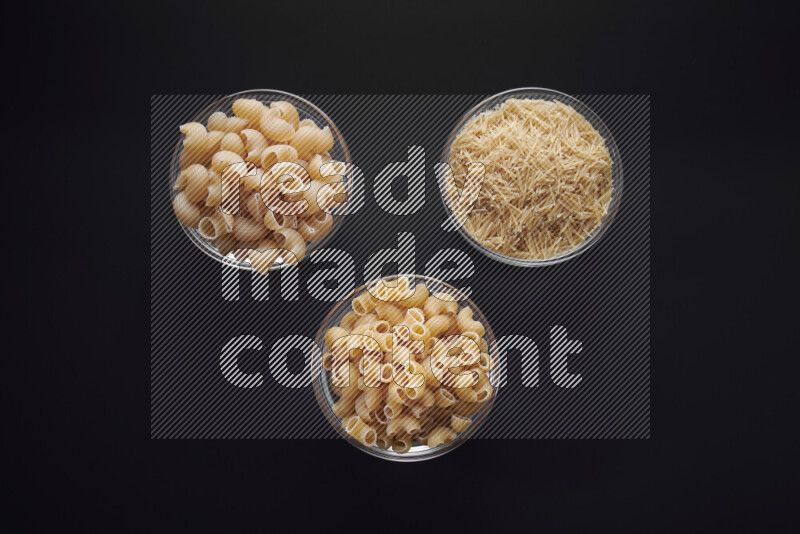 Different pasta types in glass bowls on black background