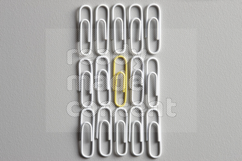 A bunch of white paper clips with a different colored paper clip in the center on grey background