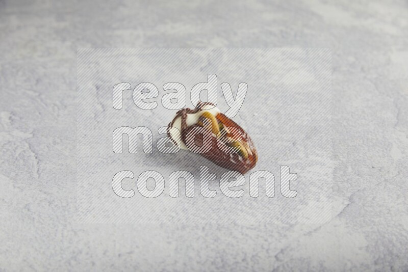 pistachio stuffed date covered with white chocolate with dark chocolate drizzle on a light grey background