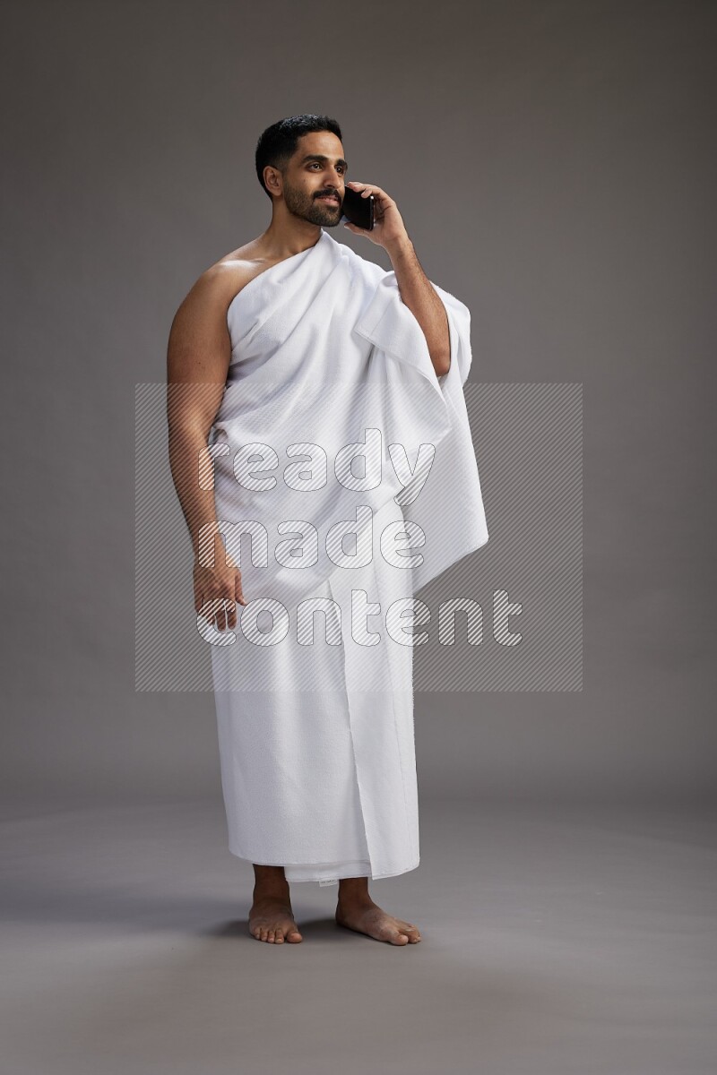 A man wearing Ehram Standing talking on phone on gray background