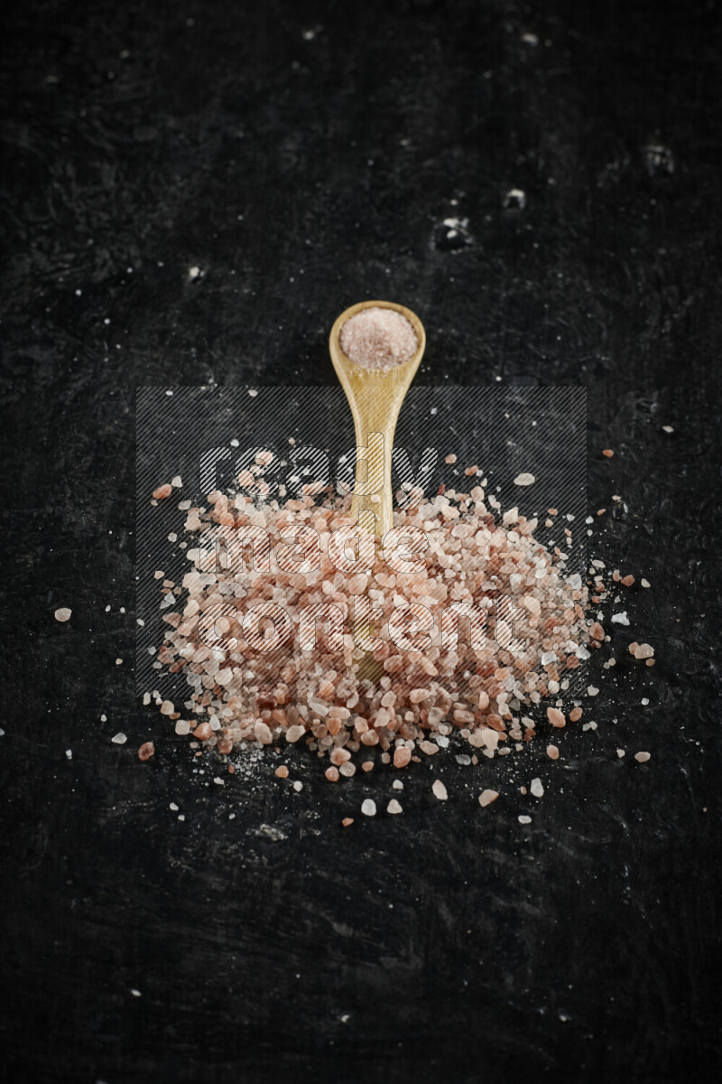 A wooden spoon full of pink himalayan salt on black background