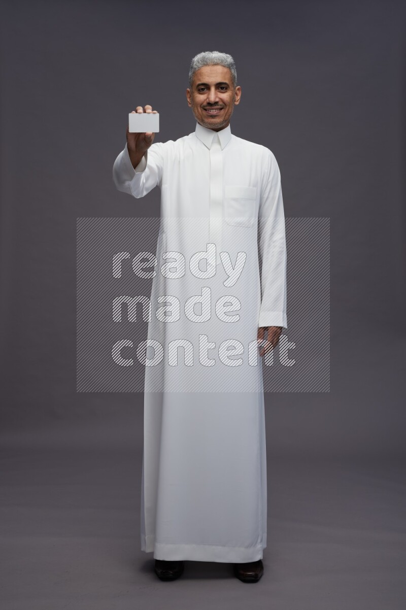 Saudi man wearing thob standing holding ATM card on gray background