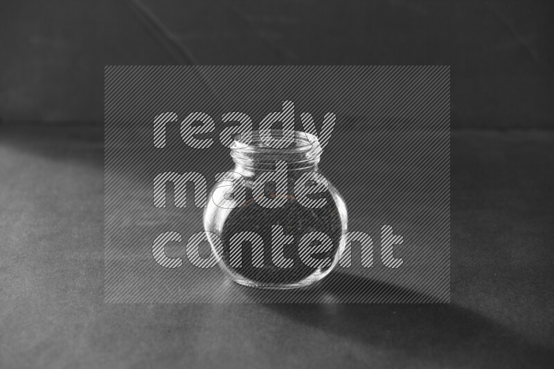 A glass spice jar full of black seeds on black flooring