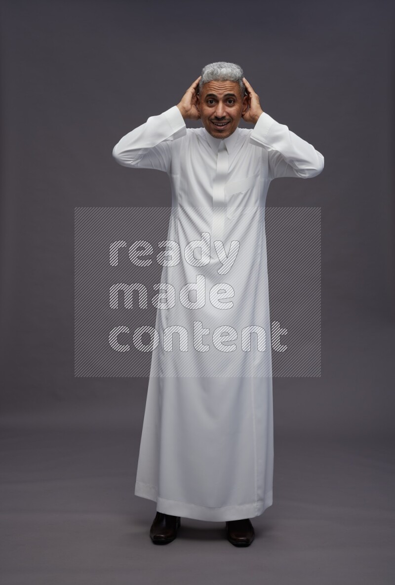 Saudi man wearing thob standing hands behind head on gray background