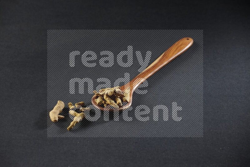 A wooden ladle full of dried turmeric fingers on black flooring