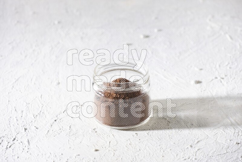 A glass jar full of cloves powder on a textured white flooring