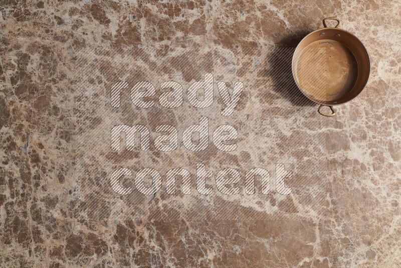 A small copper pan on beige marble background