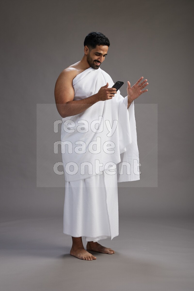 A man wearing Ehram Standing texting on phone on gray background