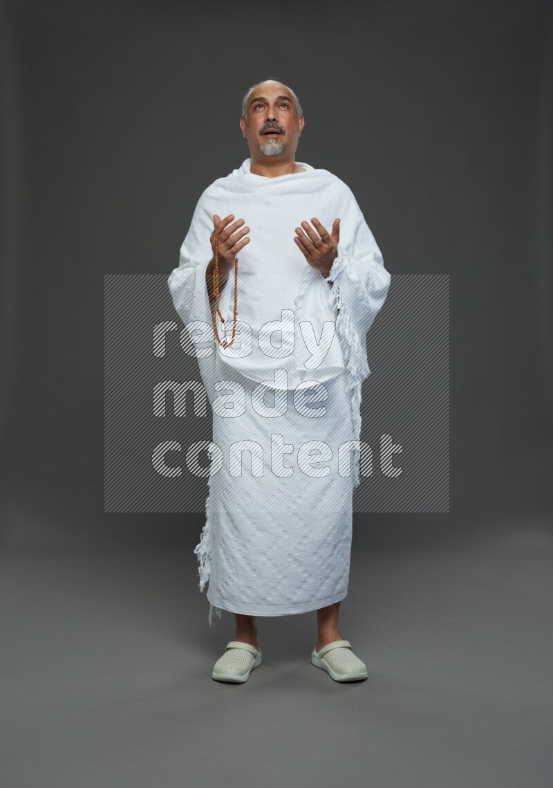A man wearing Ehram Standing dua'a on gray background