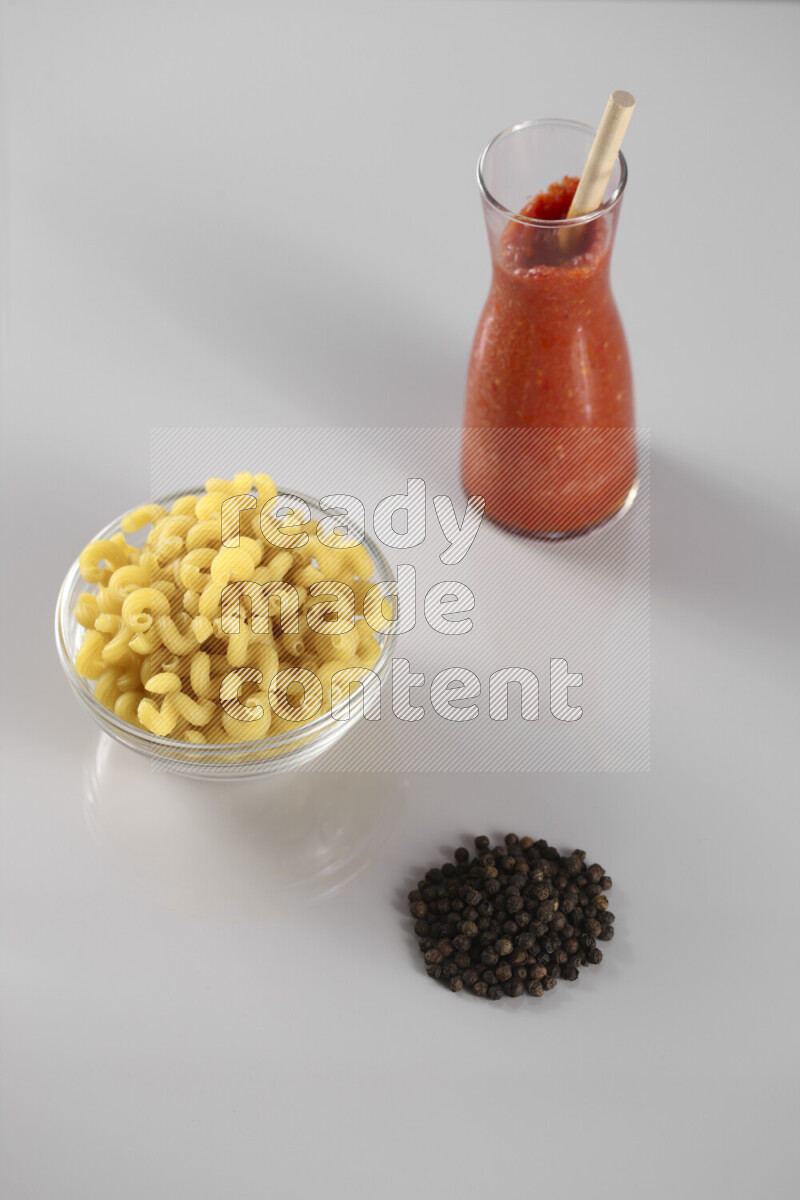 Raw pasta with tomatoe pasta with different ingredients such as cherry tomatoes, basil, garlic, bay laurel, cardamom, white pepper, black pepper, red chilis and wheat stalks on light grey background