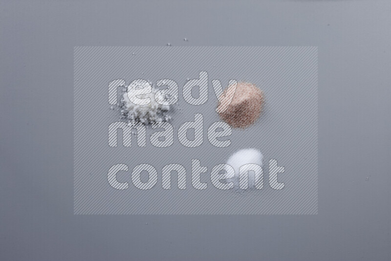 Bunches of table salt, coarse sea salt, fine himalayan salt and coarse himalayan salt on grey background