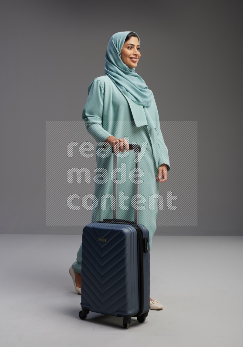 Saudi Woman wearing Abaya standing holding Travel bag on Gray background