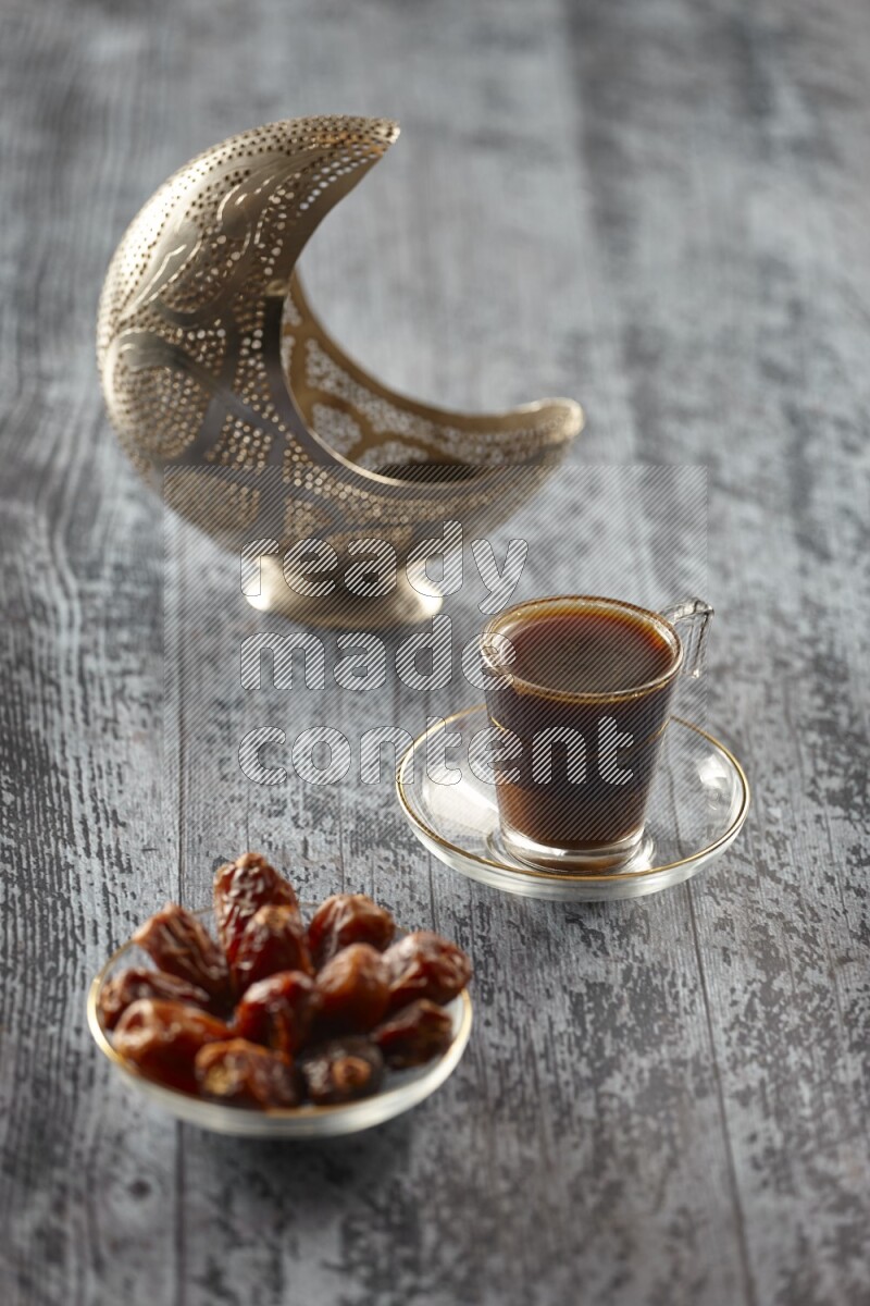A silver lantern with different drinks, dates, nuts, prayer beads and quran on grey wooden background
