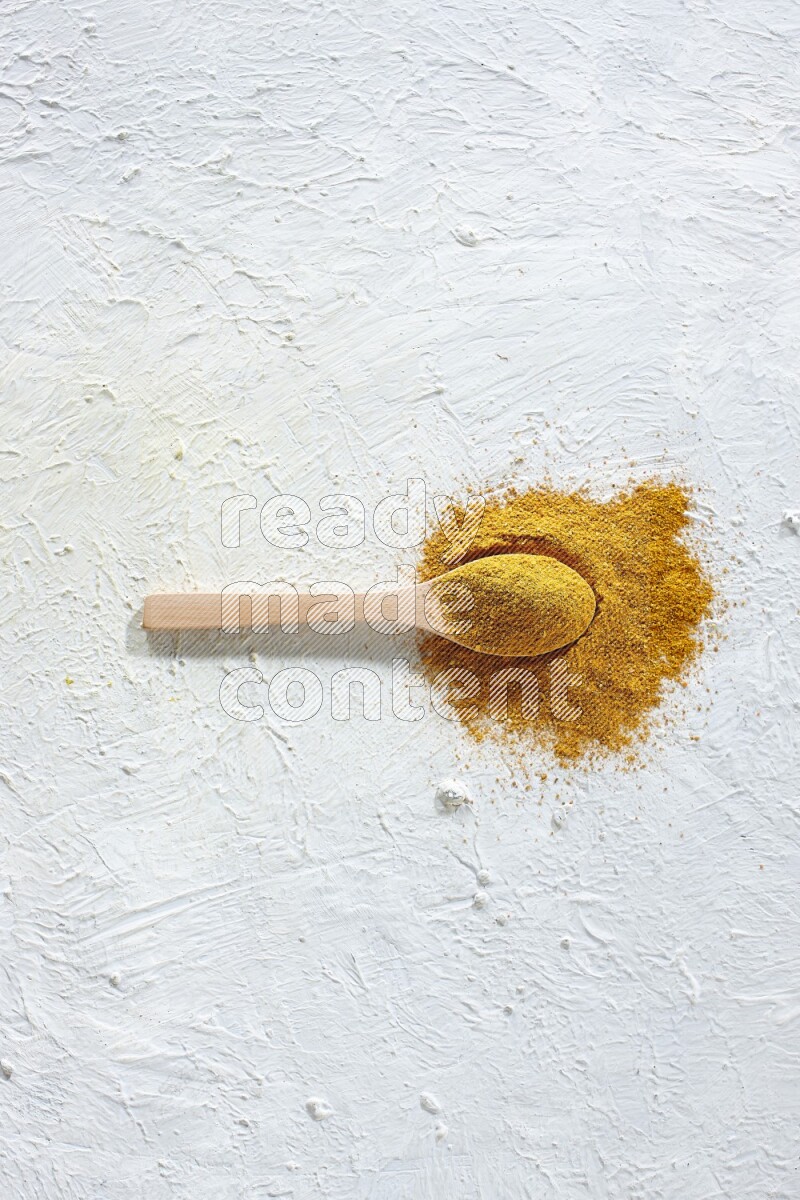 A wooden spoon full of turmeric powder on textured white background