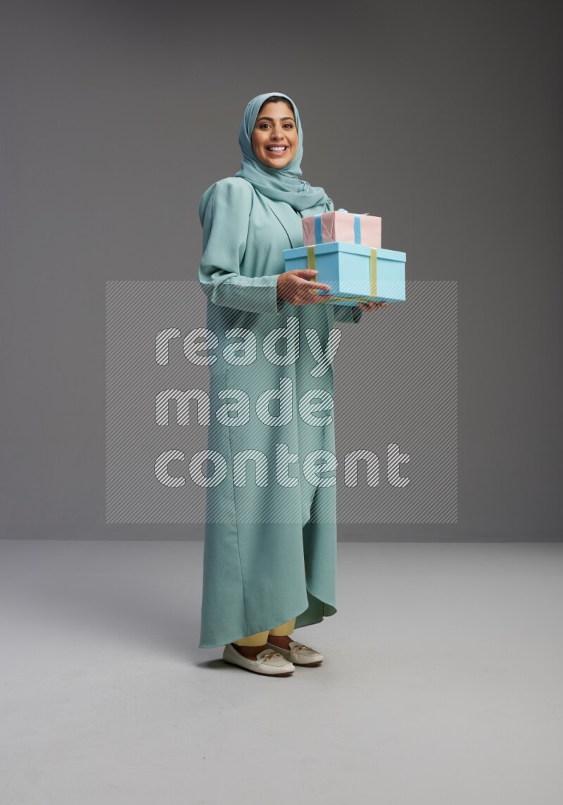 Saudi Woman wearing Abaya standing holding gift box on Gray background