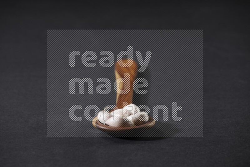 A wooden ladle full of garlic cloves on a black flooring