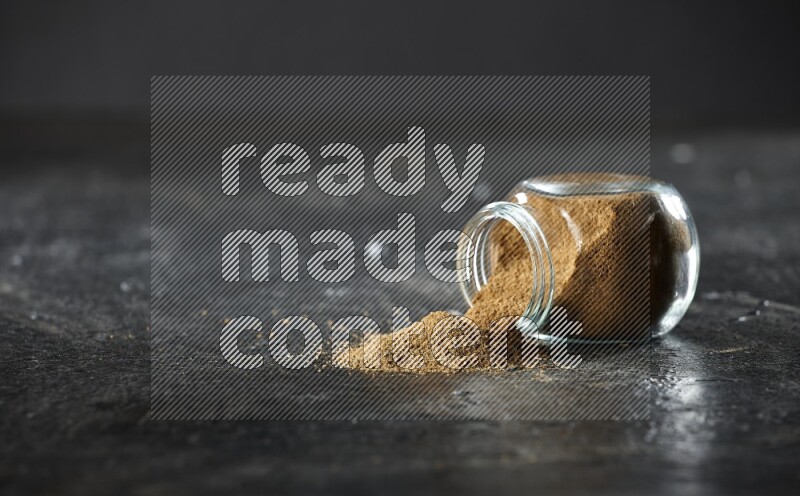 وعاء زجاجي مقلوب ممتلئ ببودرة الكمون والبودرة تناثرت منه على خلفية سوداء