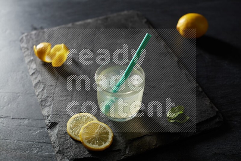 A glass of lemon juice with a straw on black background