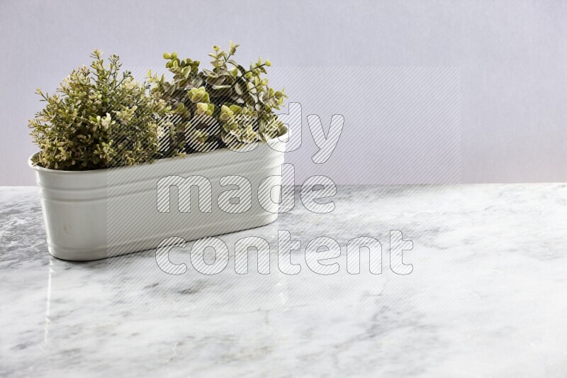 Multiple green artificial plants in white pot on grey marble background
