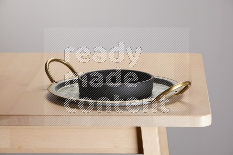 black bowl placed on a rounded stainless steel tray with golden handels on the edge of wooden table