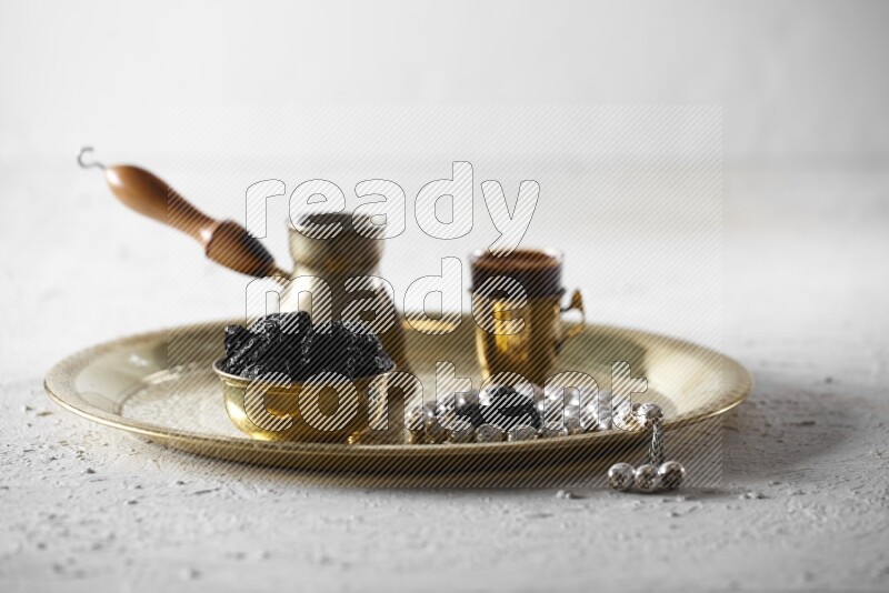 Dried plums in a metal bowl with coffee and prayer beads on a tray in a light setup