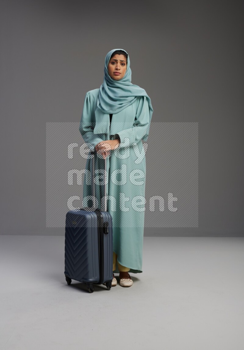 Saudi Woman wearing Abaya standing holding Travel bag on Gray background