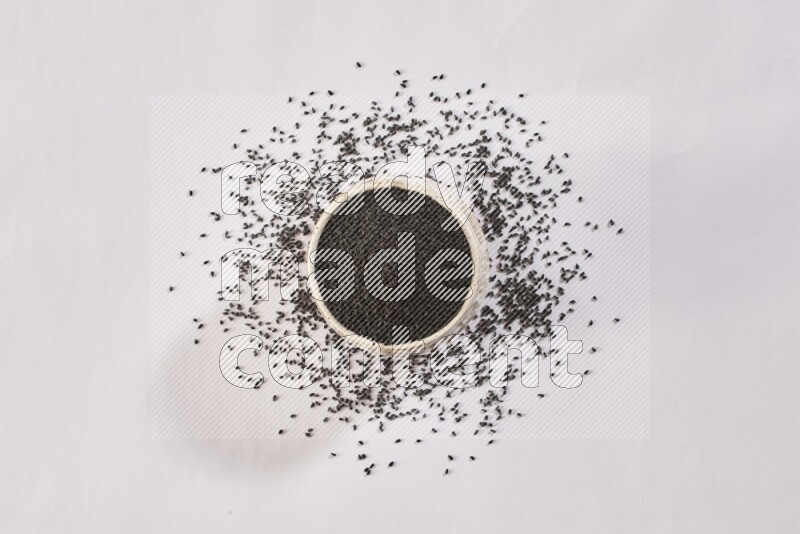 A beige pottery bowl full of black seeds and more seeds spread on a white flooring