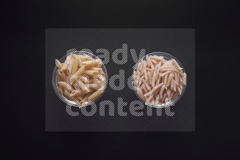 Different pasta types in glass bowls on black background