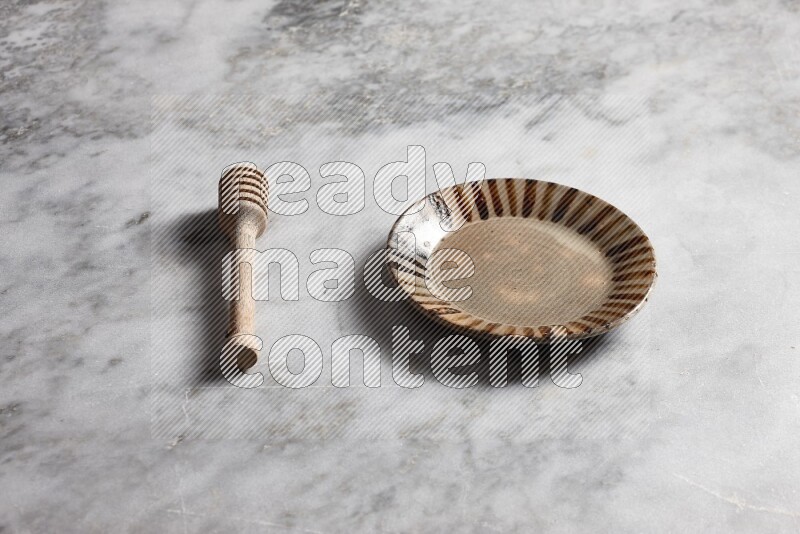 Multicolored pottery plate with wooden honey dipper on the side on grey marble background