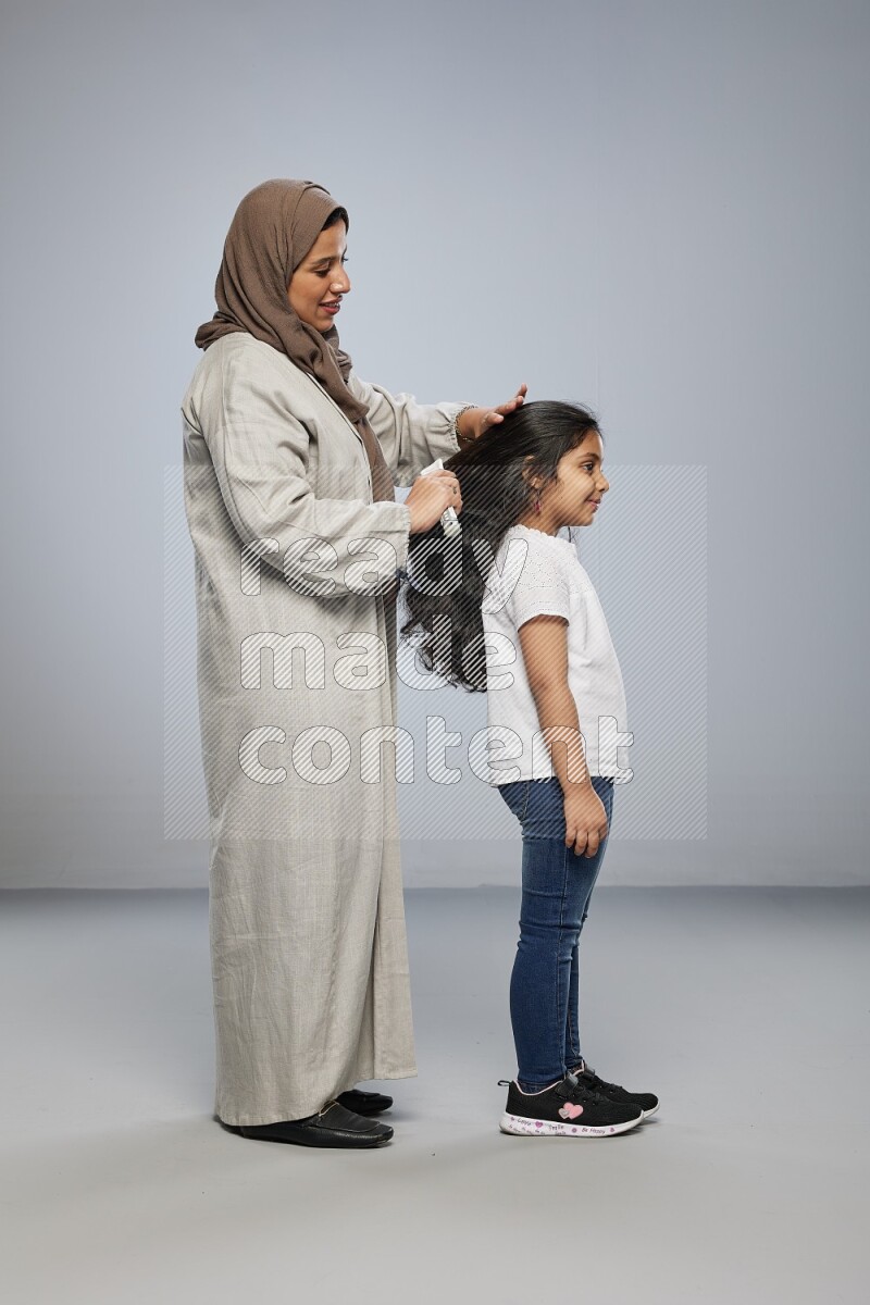 Mom standing styling hair for her daughter on gray background