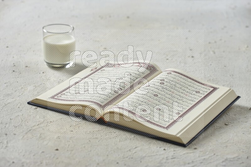 Quran with dates, prayer beads and different drinks all placed on textured white background