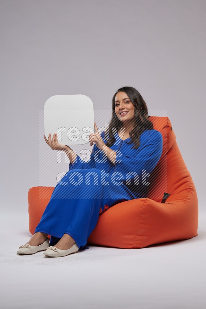 A Woman sitting on an orange beanbag wearing Jalabeya holding a social media sign