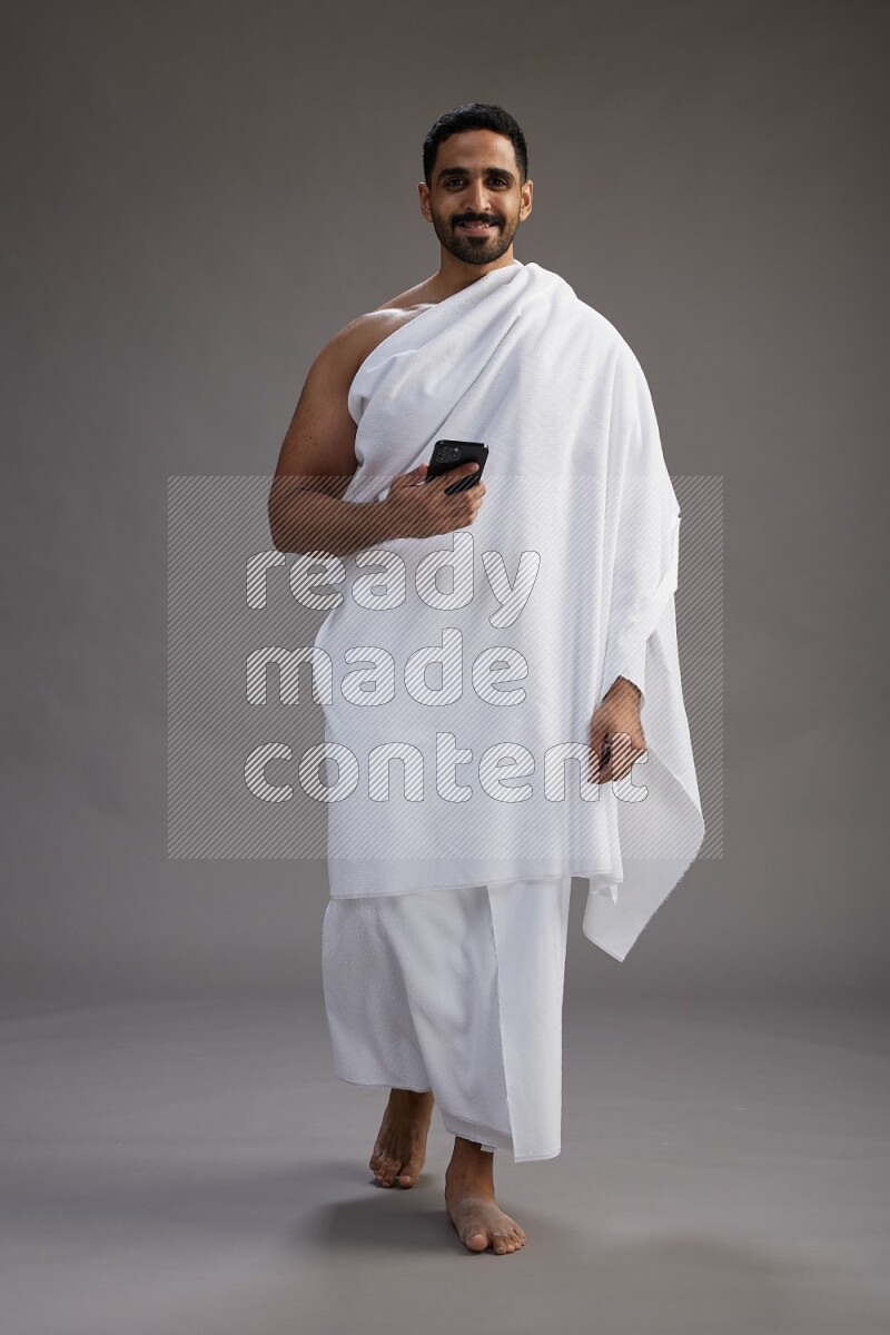 A man wearing Ehram Standing texting on phone on gray background