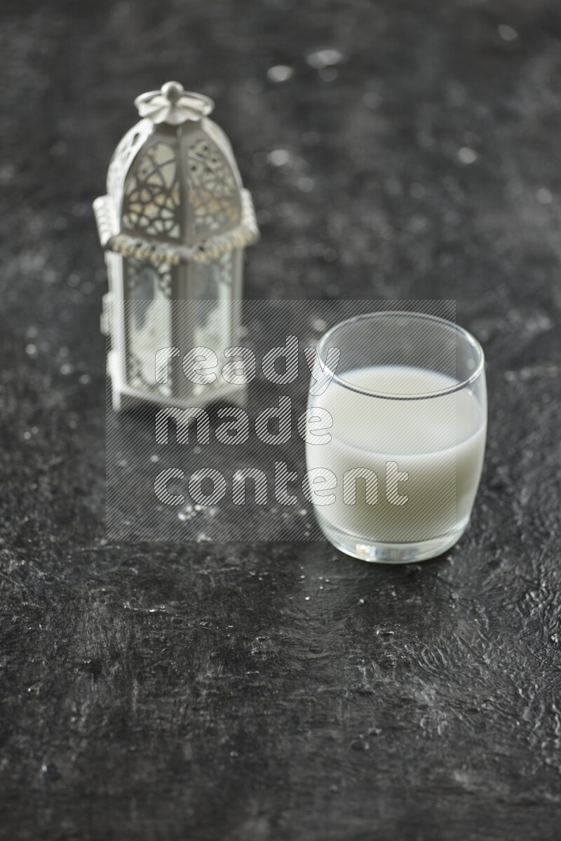 A white lantern with different drinks, dates, nuts, prayer beads and quran on textured black background