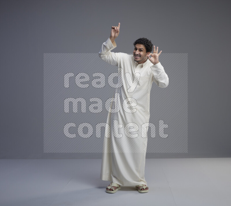 A Saudi man standing wearing thob interacting with the camera on gray background