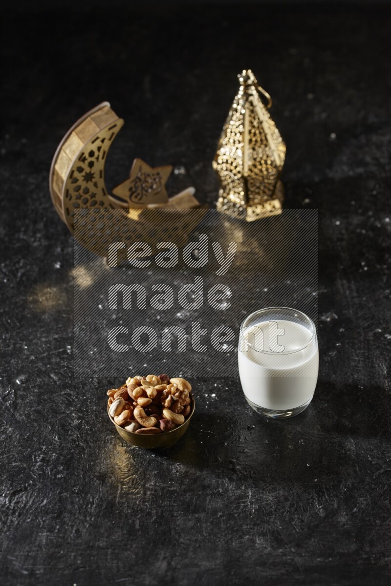 Nuts in a metal bowl with milk beside golden lanterns in a dark setup